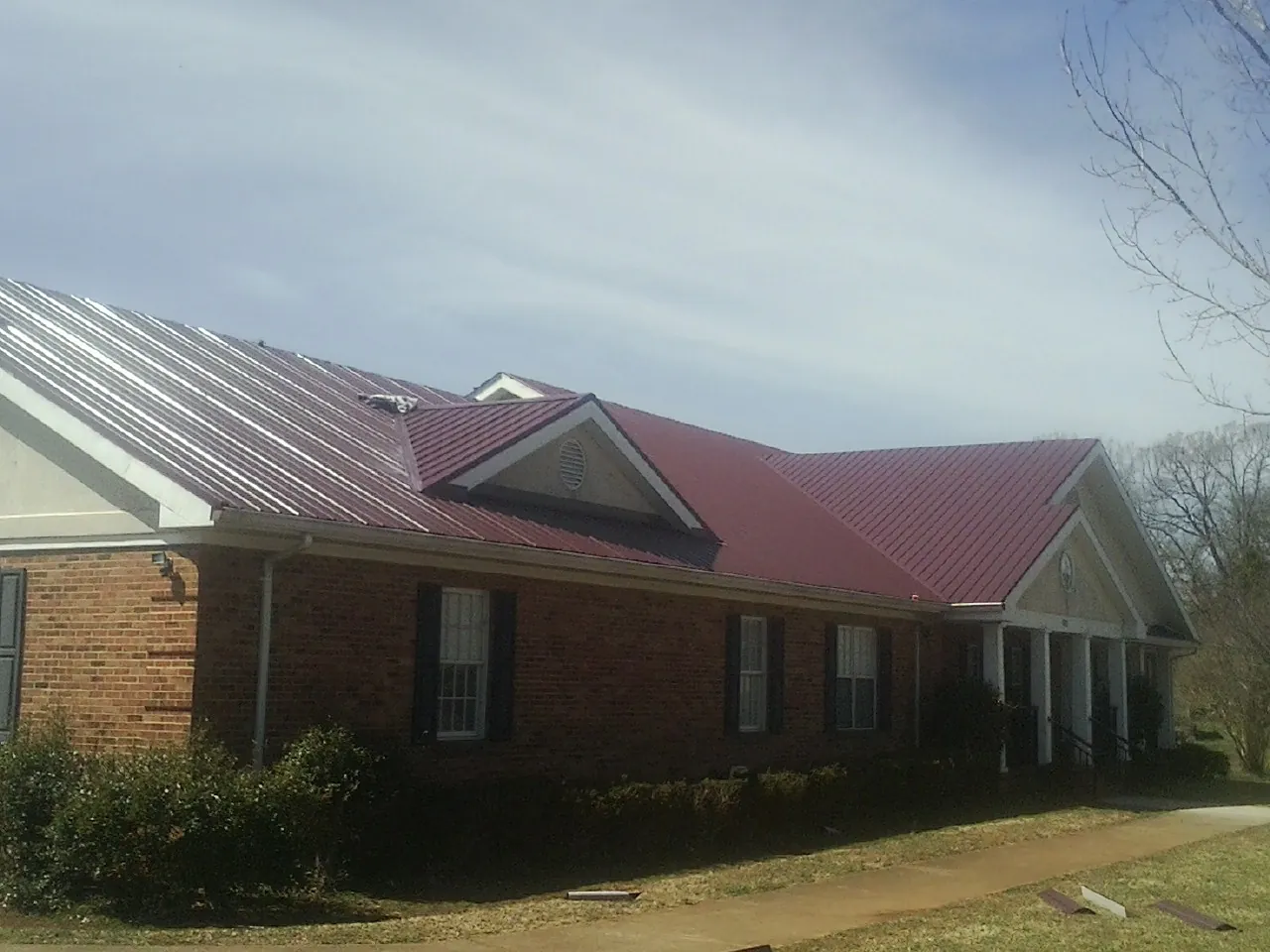 Red metal roof with gabled entries on a long brick building, from a Hail Damage Roof Repair job in Rainier