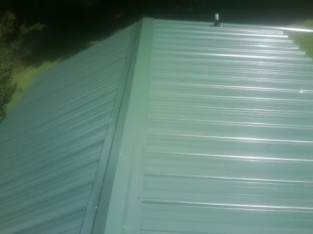 New green metal panels meeting at the ridge of a roof — Flat Roof Repair work by our crew in Rainier