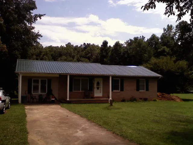 Dark green metal roof on a brick ranch with a covered porch in Rainier